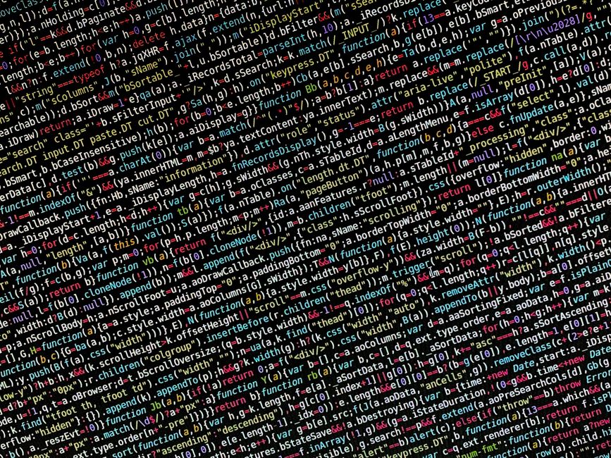 A photograph of a densely packed computer screen displaying lines of colorful programming code in various colors, including red, green, yellow, blue, and white, set against a dark background. The code